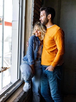 Glueckliches Paar schaut aus dem Fenster ihres Wohneigentums, welches sich noch im Bau befindet.